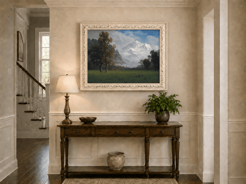 Framed hand-painted snowy mountain valley oil painting with a meadow and tall trees displayed above an entryway console table.