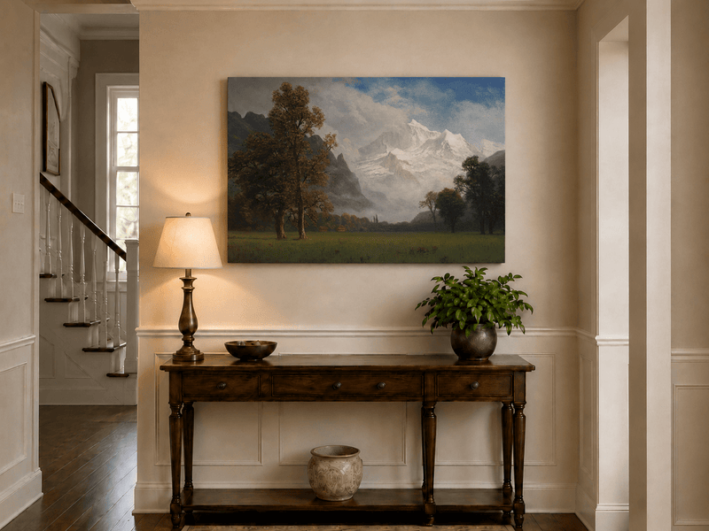 Unframed hand-painted snowy mountain valley oil painting with a meadow and tall trees displayed above an entryway console table.