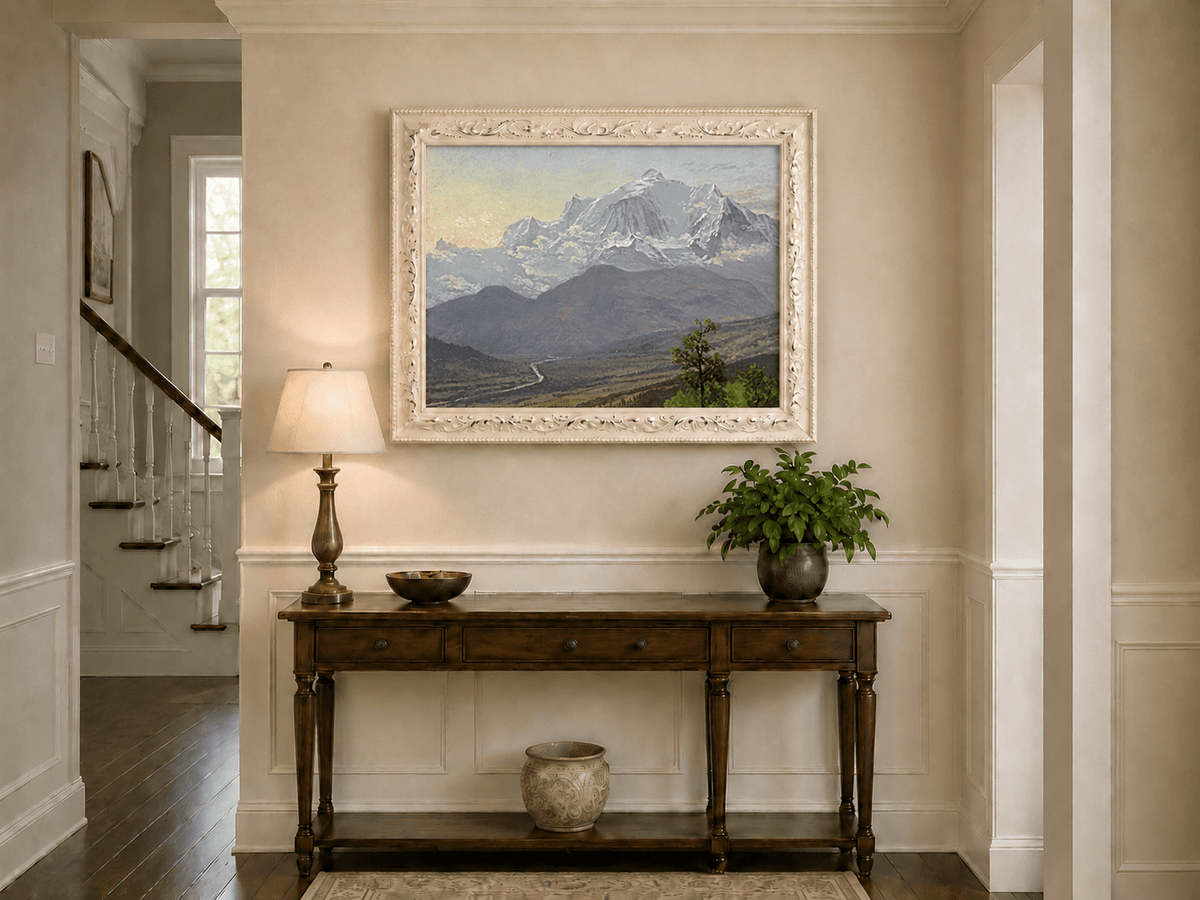 Framed hand-painted snowy mountain valley oil painting with a winding river and rolling hills displayed above an entryway console table.