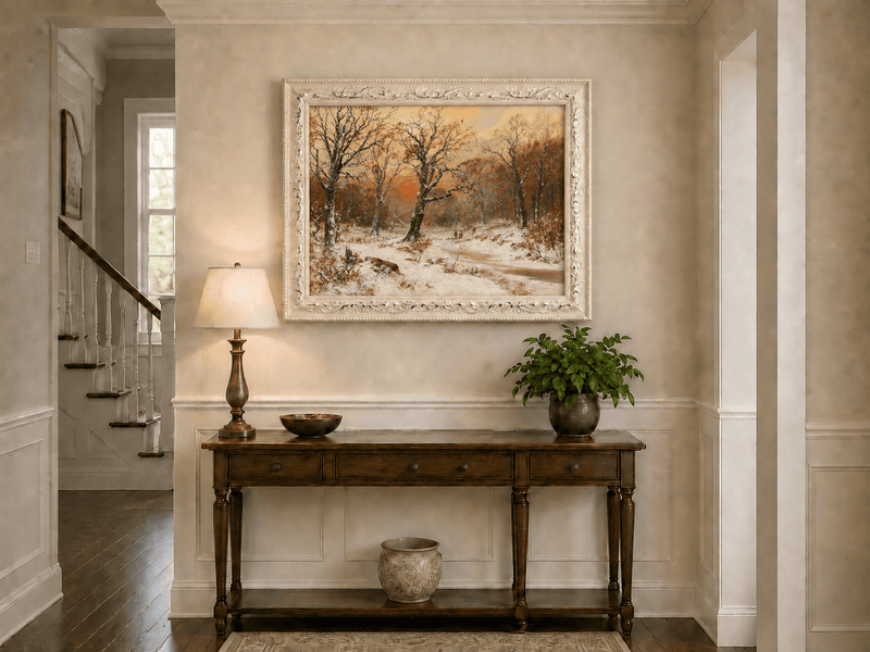 Framed hand-painted snowy woodland path oil painting beneath bare trees at sunset displayed above an entryway console table.