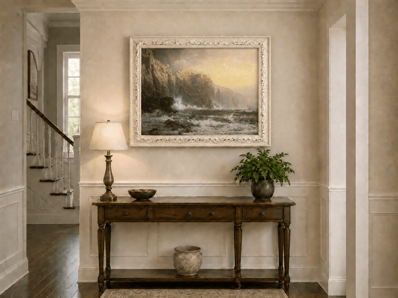 Framed hand-painted stormy seascape oil painting with a reef, surf and golden coastal cliffs displayed above an entryway console table.