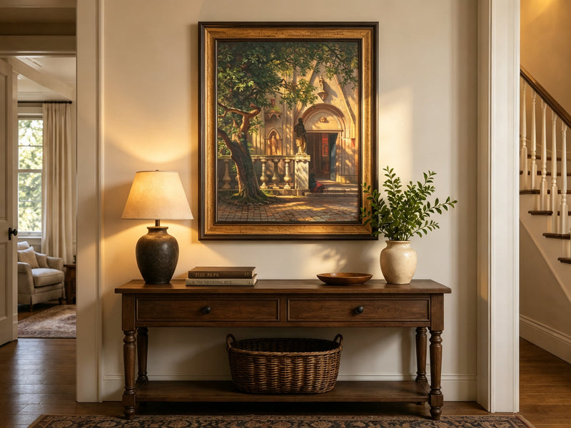 Framed hand-painted church courtyard oil painting with an old tree in warm sunlight displayed above an entryway console table.