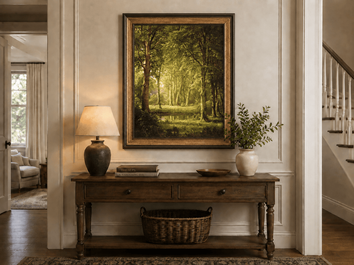 Framed hand-painted sunlit forest pond oil painting with tall trees and golden reflections displayed above an entryway console table.