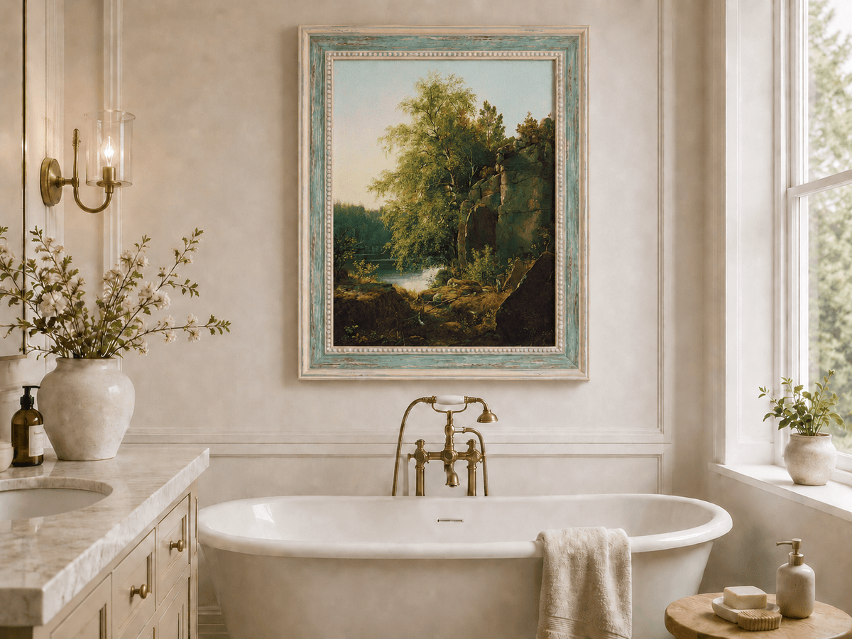 Framed hand-painted sunlit lakeside oil painting with rocks and leafy birch trees displayed above a freestanding bathtub.