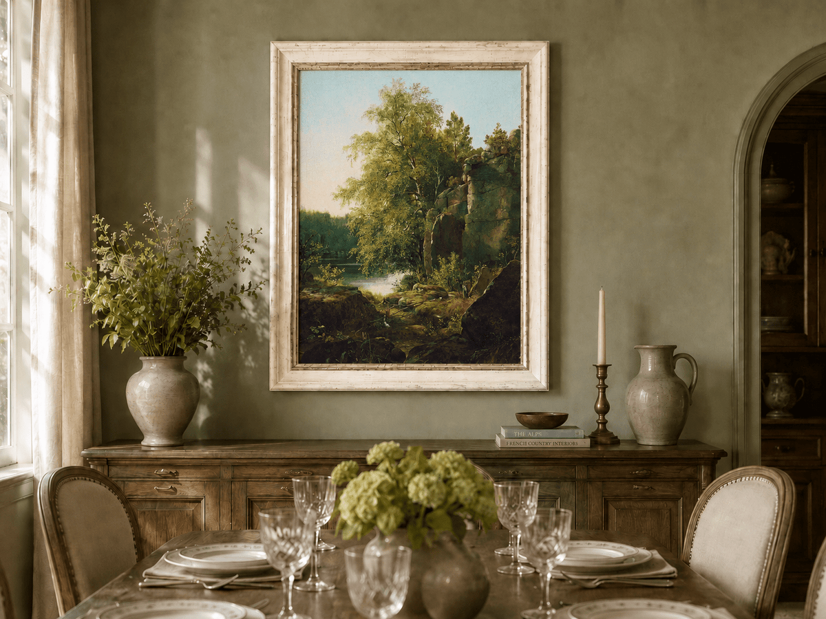 Framed hand-painted sunlit lakeside oil painting with rocks and leafy birch trees displayed above a formal dining table.