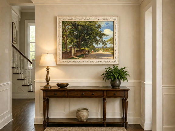Framed hand-painted country road oil painting with figures beneath broad leafy trees displayed above an entryway console table.