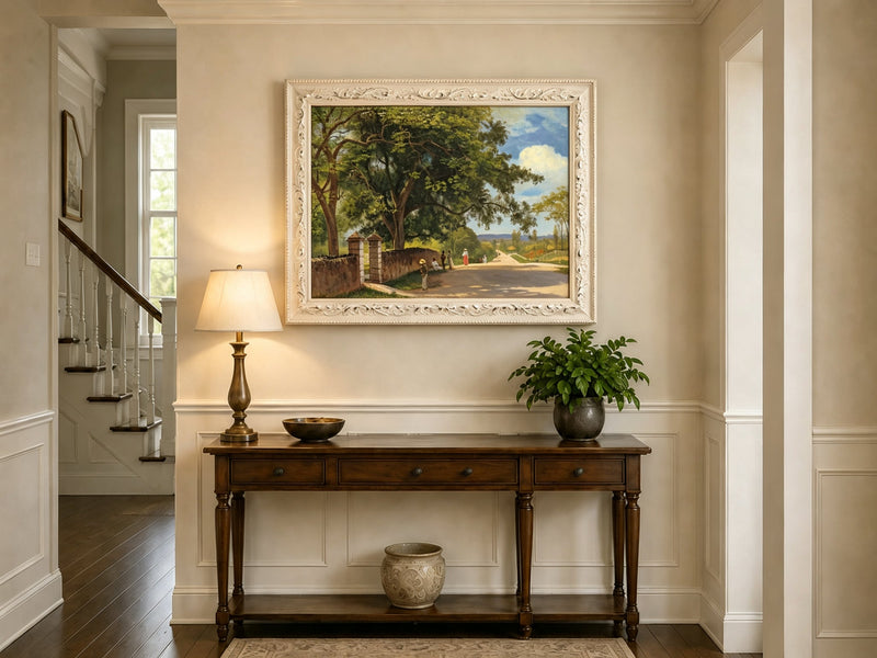 Framed hand-painted country road oil painting with figures beneath broad leafy trees displayed above an entryway console table.