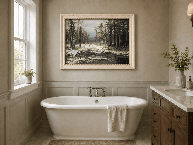 Framed hand-painted winter forest oil painting with a flowing stream through snowy woods displayed above a freestanding bathtub.