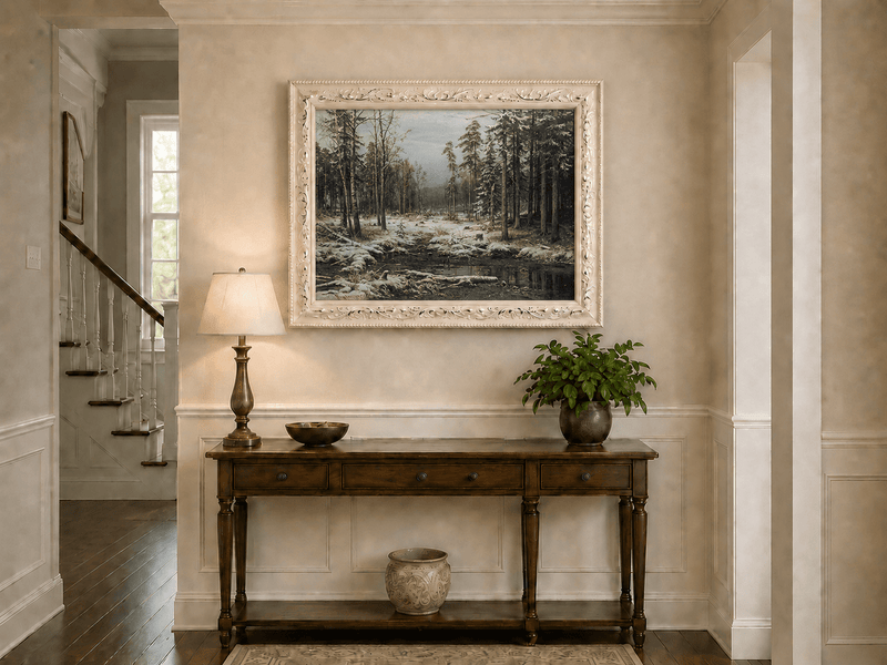 Framed hand-painted winter forest oil painting with a flowing stream through snowy woods displayed above an entryway console table.